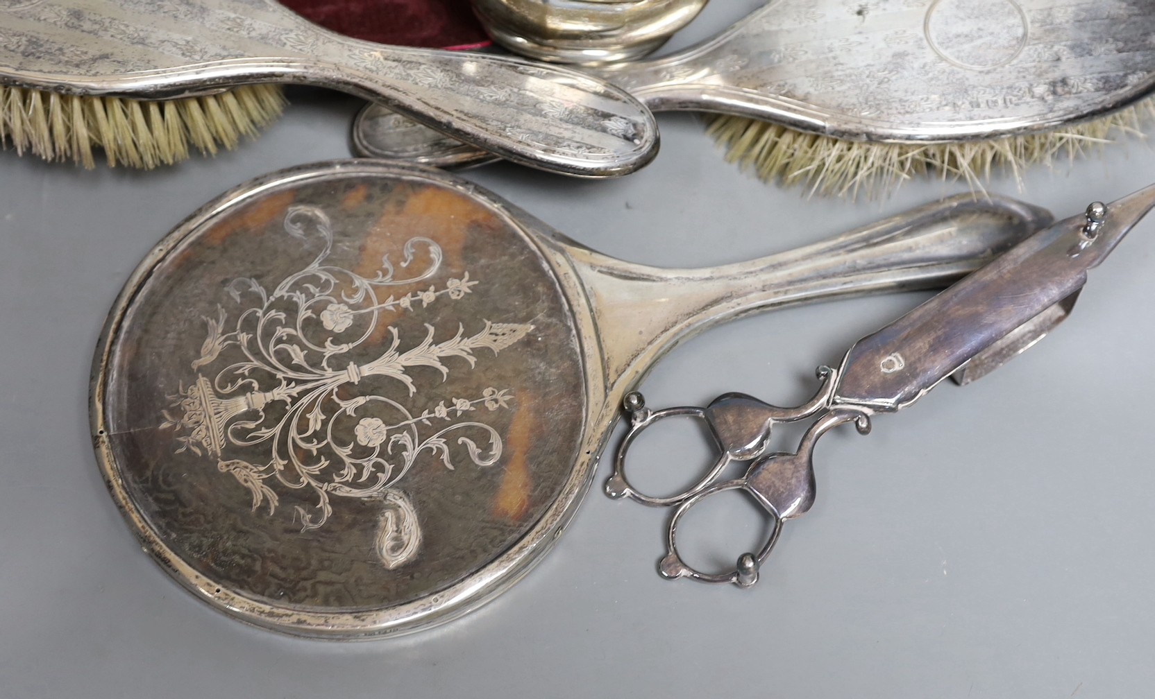 A small group of silver items including a tortoiseshell mounted hand mirror, London, 1917, two silver mounted clothes brushes, a cased set of six teaspoons, a mug and sugar bowl, together with a pair of plated candle snu